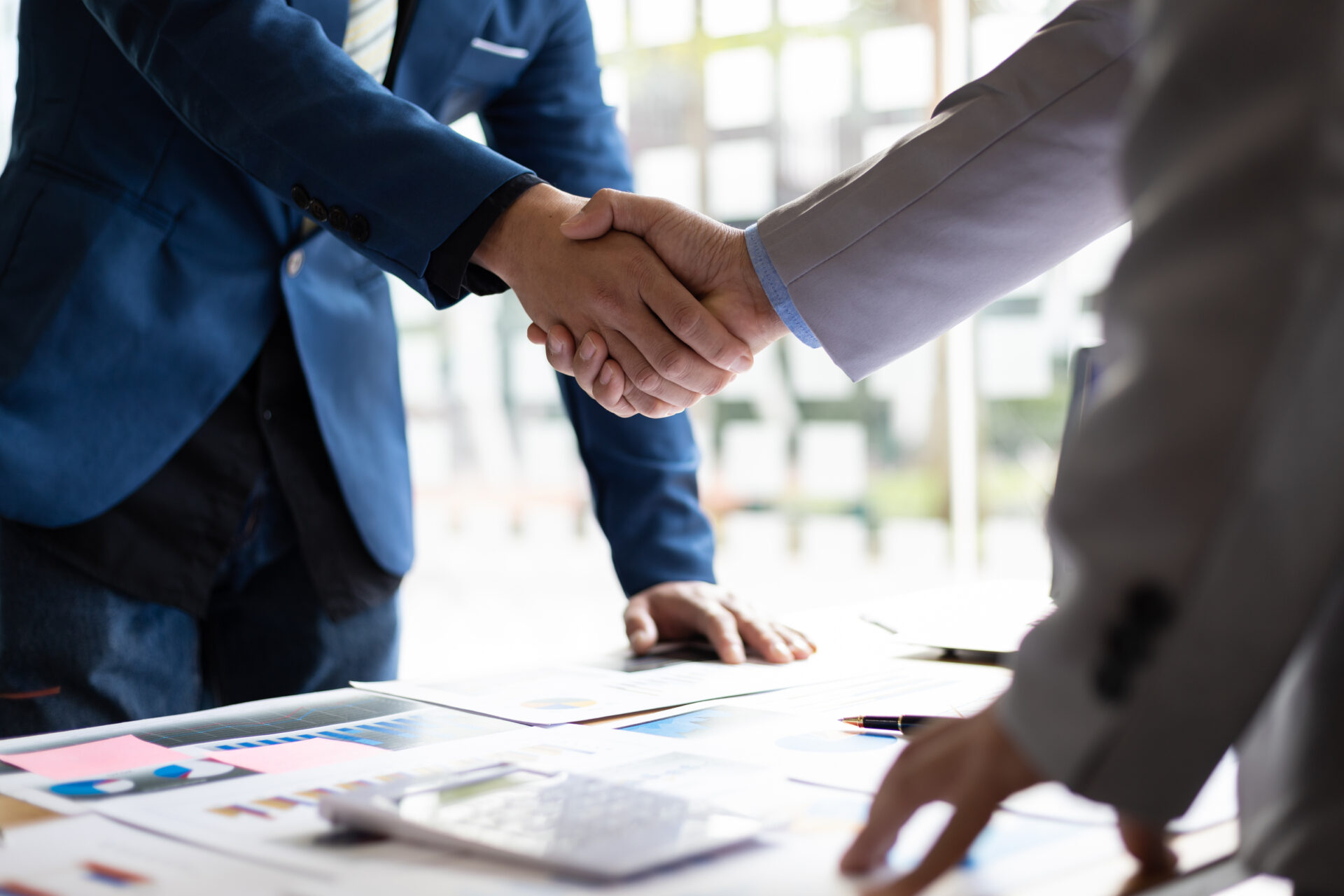 Two men shaking hands over a table with papers.